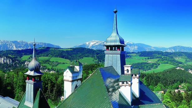 Blick auf die grüne Landschaft und die schneebedeckten Berge von einem Schloss aus.