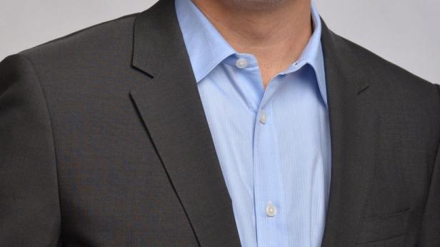 Ein Mann mit grauen Haaren trägt ein dunkles Sakko und ein hellblaues Hemd.