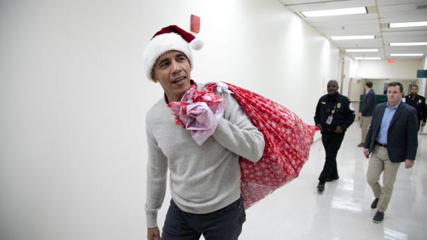 Barack Obama trägt einen Weihnachtsmannhut und einen Sack voller Geschenke.