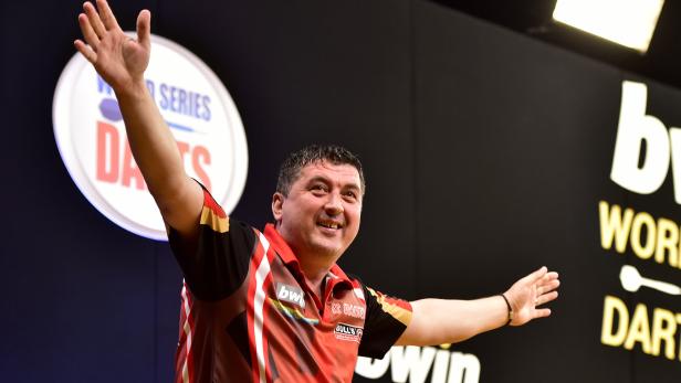 Ein Dartspieler jubelt mit erhobenen Armen auf der Bühne.