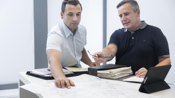 Zwei Männer beugen sich über Baupläne auf einem Tisch.