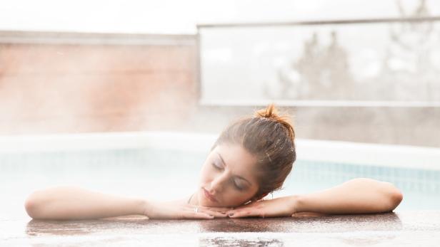 Eine Frau entspannt sich in einem Außenpool mit geschlossenen Augen.