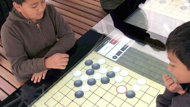Zwei Jungen spielen das Brettspiel Go auf einem digitalen Tisch.
