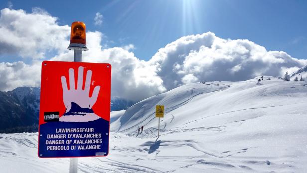 Ein Lawinengefahr-Schild mit Warnblinkanlage steht auf einer schneebedeckten Berglandschaft.