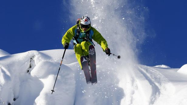 Ein Skifahrer springt über eine schneebedeckte Klippe vor blauem Himmel.