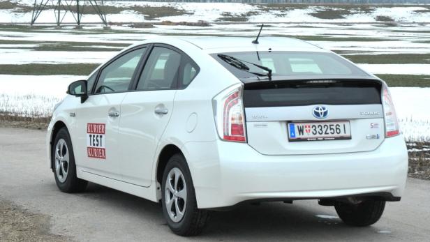 Ein weißer Toyota Prius mit dem Aufdruck „Kurier Test“ auf der Seite steht auf einer Straße.