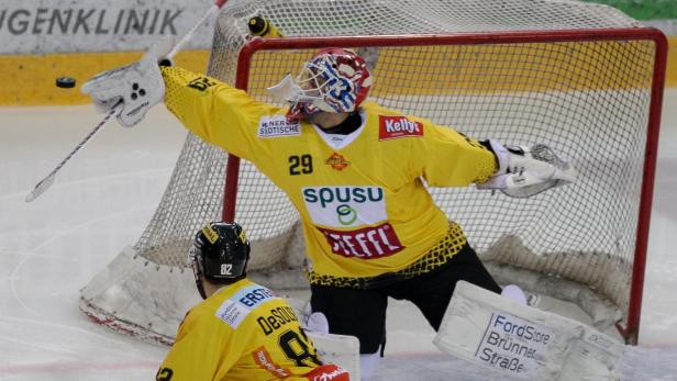 Ein Eishockeytorwart in gelber Ausrüstung wehrt einen Puck ab.