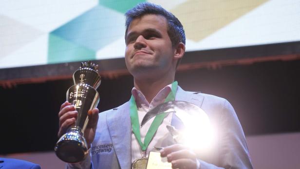 Magnus Carlsen hält zwei Trophäen in den Händen.