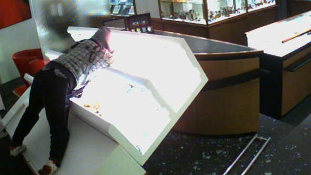 Eine Person beugt sich über eine zerbrochene Vitrine in einem Geschäft.