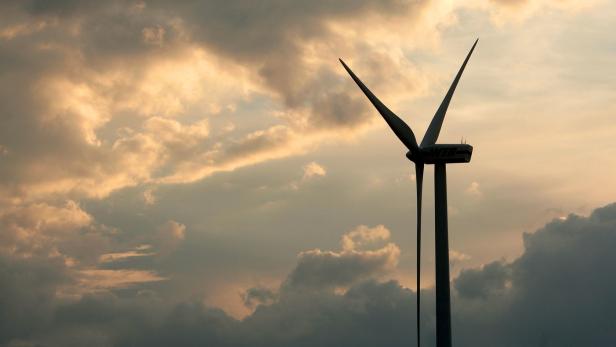 Eine Windkraftanlage vor einem bewölkten Himmel bei Sonnenuntergang.