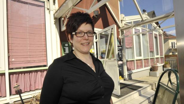 Eine Frau mit Brille steht vor einem Gebäude mit einem Schild mit der Aufschrift „Information“.