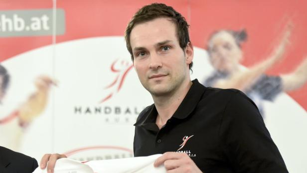 Ein Mann im schwarzen Poloshirt hält ein weißes Trikot in den Händen.