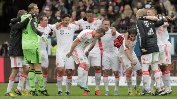 Eine Gruppe Fußballspieler des FC Bayern München umarmt sich auf dem Spielfeld.