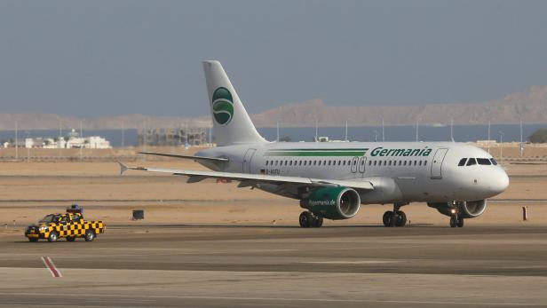 Ein Flugzeug der Germania rollt auf einer Startbahn, begleitet von einem gelb-schwarz karierten Fahrzeug.
