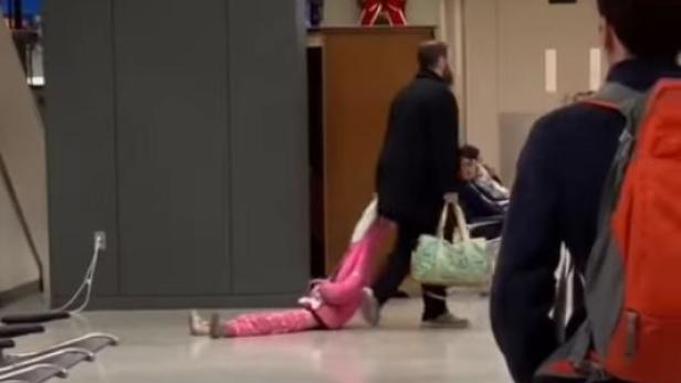 Ein Mann zieht ein Kind in rosa Kleidung am Flughafen hinter sich her.