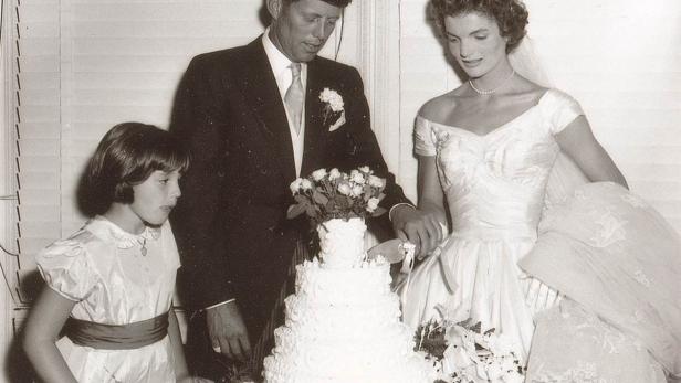 John F. Kennedy und Jacqueline Bouvier schneiden ihre Hochzeitstorte an, während ein junges Mädchen zusieht.