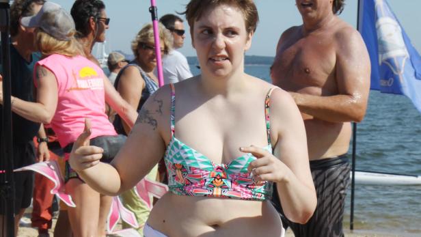 Lena Dunham am Strand, umgeben von anderen Menschen.