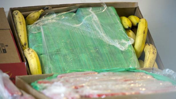 Ein Karton mit Bananen und einem in Folie verpackten, grünen Gegenstand.