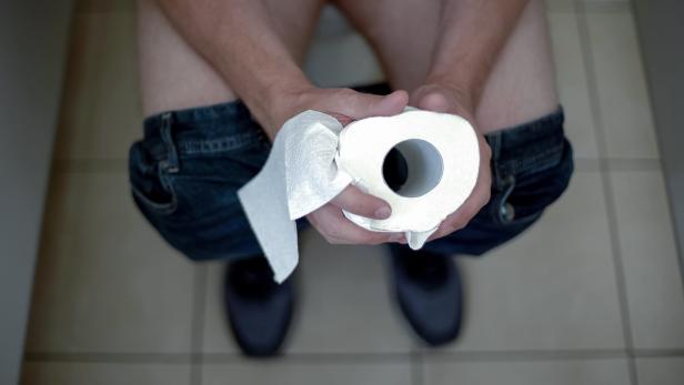 Mensch sitzt ohne Klohocker auf dem WC und hält Toilettenpapier