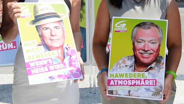 Zwei Personen halten Wahlplakate der Grünen mit den Slogans „Nur nicht bewegen, wenn’s heiß wird“ und „Hawedere, Atmosphäre!“.