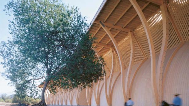 Zwei Reiter reiten an einem Gebäude mit einer Fassade aus hellem Holz entlang.