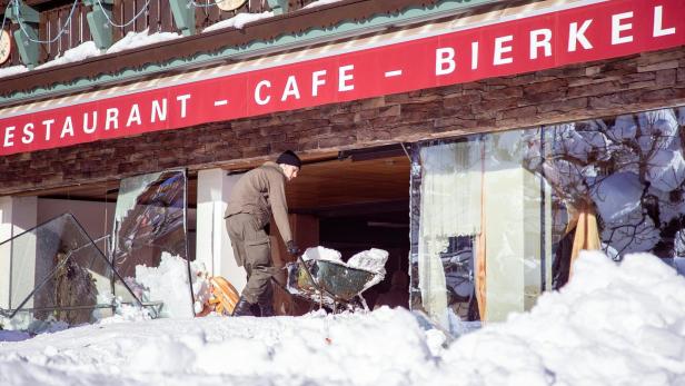 Ein Mann schiebt eine Schubkarre voller Schnee vor einem beschädigten Restaurant.