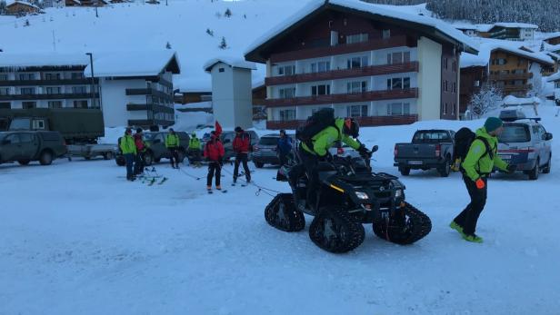 Ein Quad zieht eine Gruppe Skifahrer auf einer verschneiten Fläche.