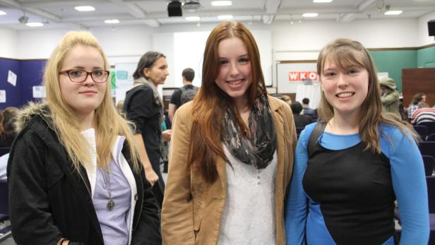 Drei junge Frauen posieren lächelnd für ein Foto in einem Konferenzraum.