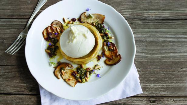 Burrata mit Artischocke, Pilzen, Pesto und Pinienkernen auf einem Teller.