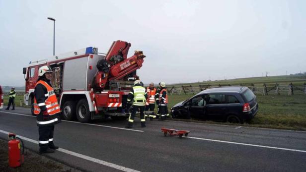 Ein Feuerwehrauto und Einsatzkräfte stehen neben einem verunglückten Auto auf einer Landstraße.