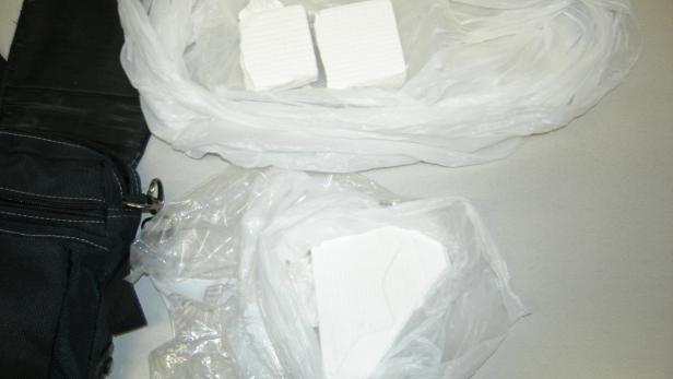 Eine schwarze Tasche und mehrere in Plastik verpackte, weiße Blöcke liegen auf einem Tisch.