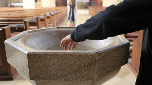 Katholischer Priester fasst ins Taufbecken