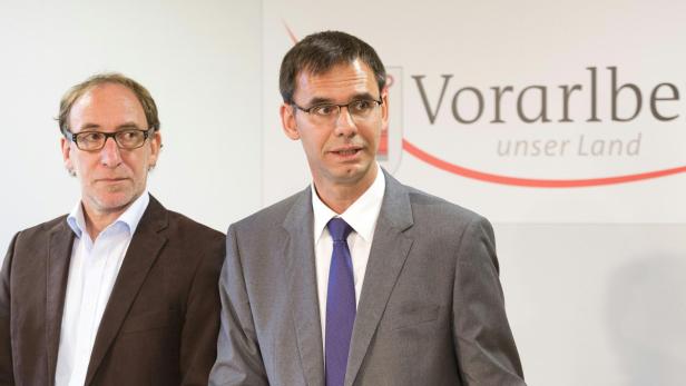 Zwei Männer in Anzügen stehen vor einem Vorarlberg-Logo.