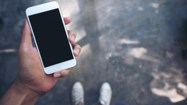 Eine Person hält ein Smartphone mit schwarzem Bildschirm in der Hand.