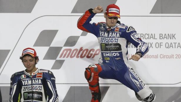 Zwei MotoGP-Fahrer auf dem Podium, einer jubelt in Yamaha-Rennbekleidung.