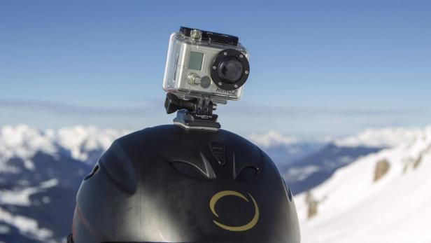 Eine GoPro-Kamera ist an einem schwarzen Skihelm befestigt, im Hintergrund schneebedeckte Berge.