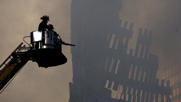 Feuerwehrleute auf einer Drehleiter vor einem teilweise zerstörten Gebäude.