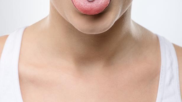Frau streckt die Zunge heraus, auf der eine Aspirinpille liegt