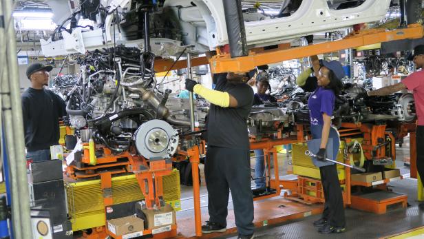 Mehrere Arbeiter montieren ein Auto in einer Fabrikhalle.