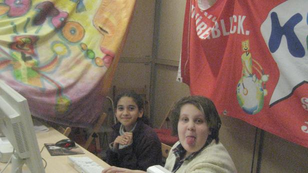 Zwei Mädchen sitzen vor einem Computer unter bunten Bannern.