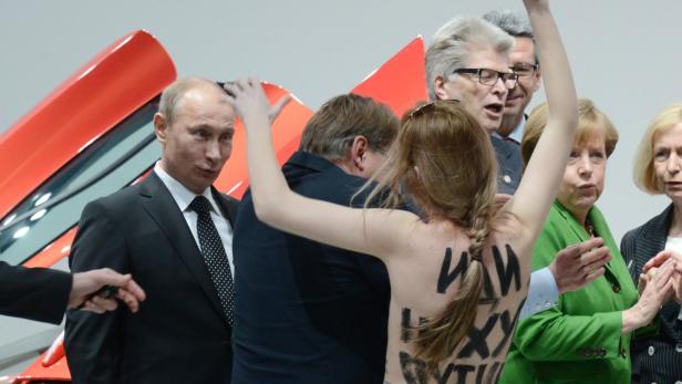 epa03653603 An eye-opening experience for Russian President Vladimir Putin (left) as he is confronted by a topless demonstrator with written messages on her back during an opening tour of the Hanover Fair, Hanover, Germany 8 April 2013. He was accomoanied by German Chancellor Angela Merkel (seen right). EPA/JOCHEN LUEBKE