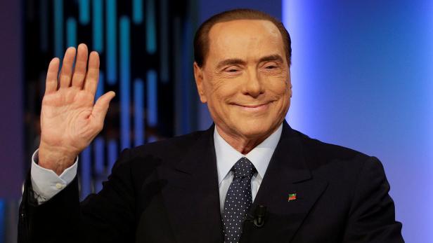 Silvio Berlusconi lächelt und hebt die Hand.