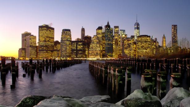 Die Skyline von Manhattan leuchtet in der Abenddämmerung hinter alten Anlegestellen.