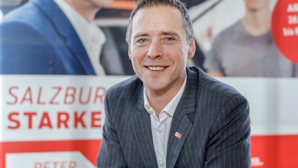 Peter Eder posiert vor einem Wahlplakat in Salzburg.