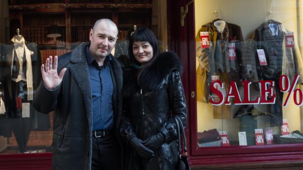 Ein Mann und eine Frau posieren vor einem Schaufenster mit dem Hinweis „Sale“.
