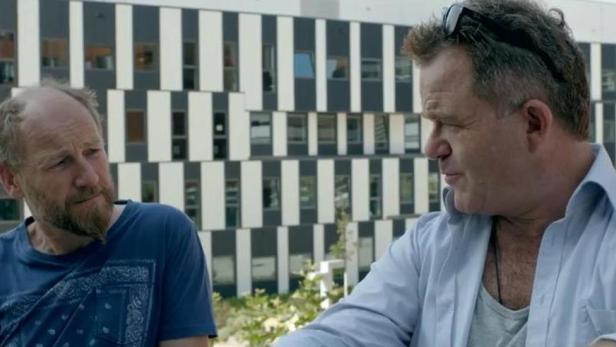 Zwei Männer unterhalten sich vor einem Gebäude mit schwarz-weißen Streifen.