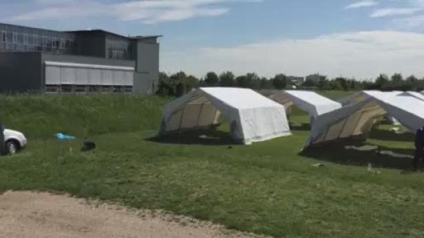 Mehrere weiße Zelte stehen auf einer Wiese vor einem Gebäude.