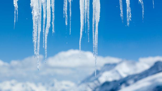 Eiszapfen hängen vor einem blauen Himmel und schneebedeckten Bergen.