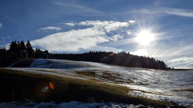 Eine teilweise schneebedeckte Wiese unter einem strahlend blauen Himmel mit Sonne.