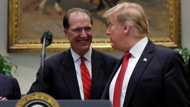 Donald Trump mit einem lächelnden Mann hinter einem Rednerpult mit dem Siegel des Präsidenten.